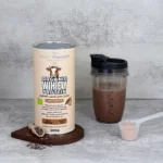 Shaker containing whey protein shake next to a can of organic whey protein powder with cacao